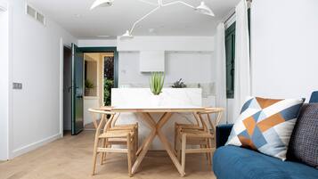 Una sala de estar moderna con un sofá azul, una mesa de comedor de madera con dos sillas y un tapete estampado.