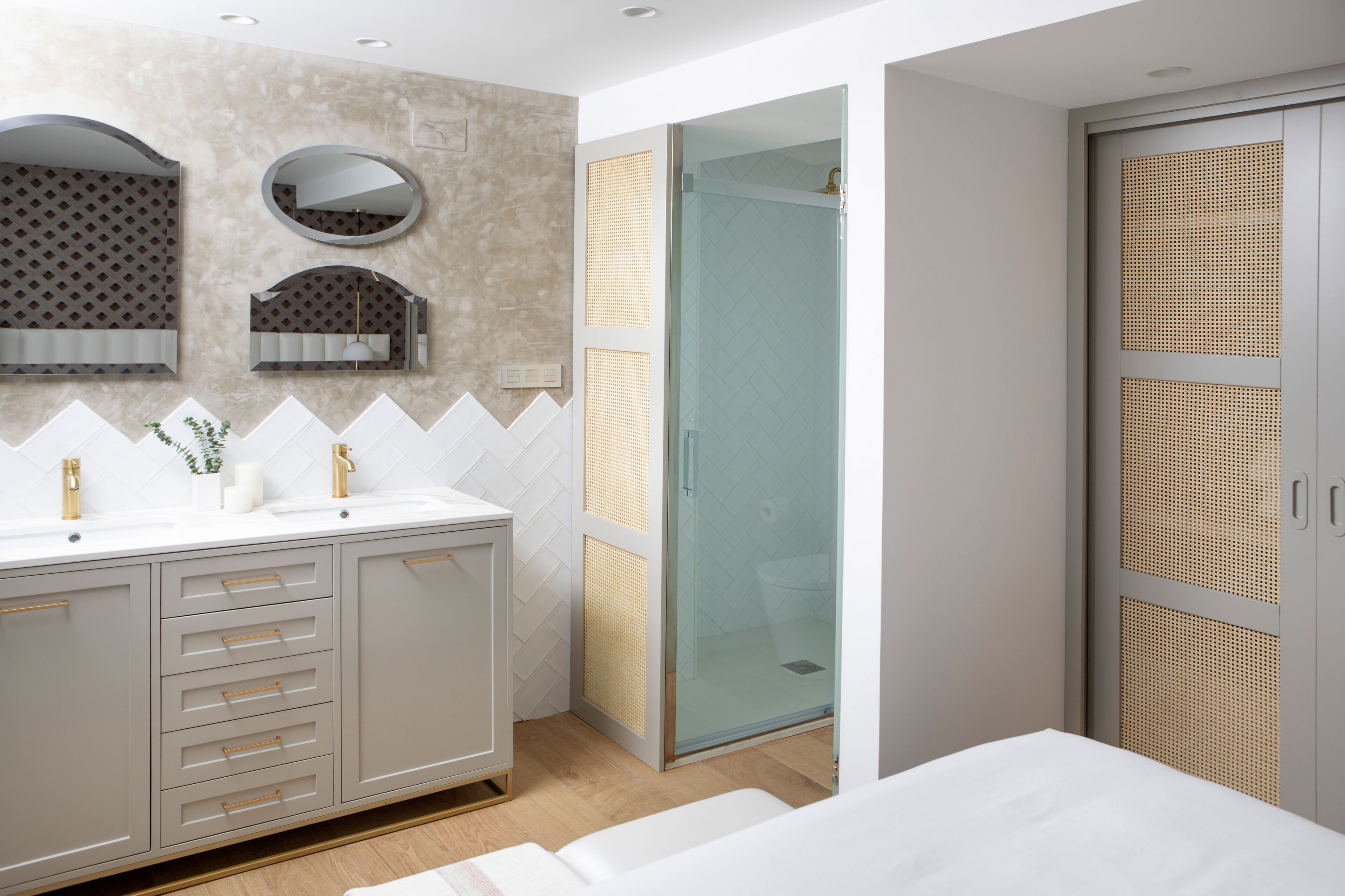 A modern bathroom with a large vanity, a glass shower enclosure, and a walk-in closet with a woven door.