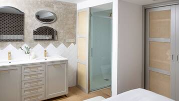 A modern bathroom with a large vanity, a glass shower enclosure, and a walk-in closet with a woven door.