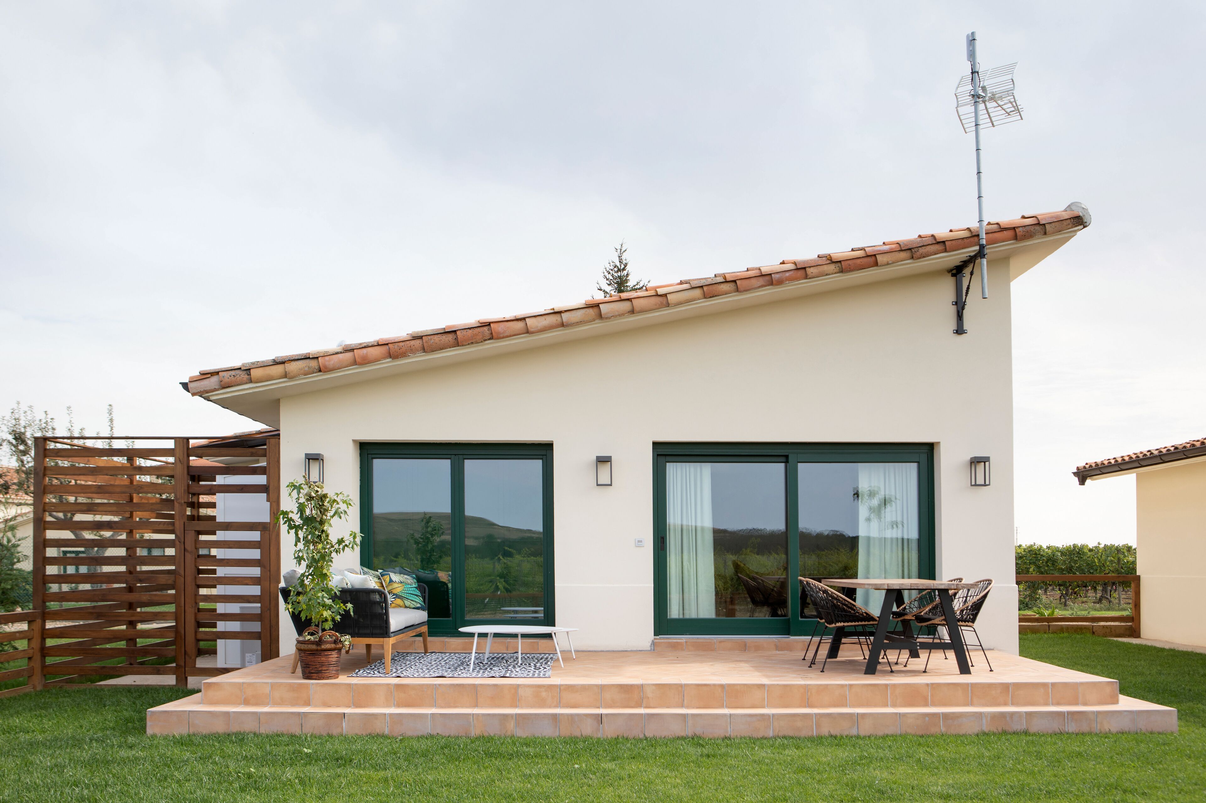 A modern house with a patio, a dining area with outdoor furniture, and a large sliding glass door.