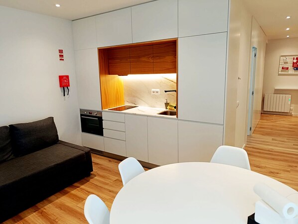 A modern kitchen with white cabinets, a wooden countertop, and a built-in oven. There is a dining area with a white table and chairs. - Cavalos de Ofir (Fão)