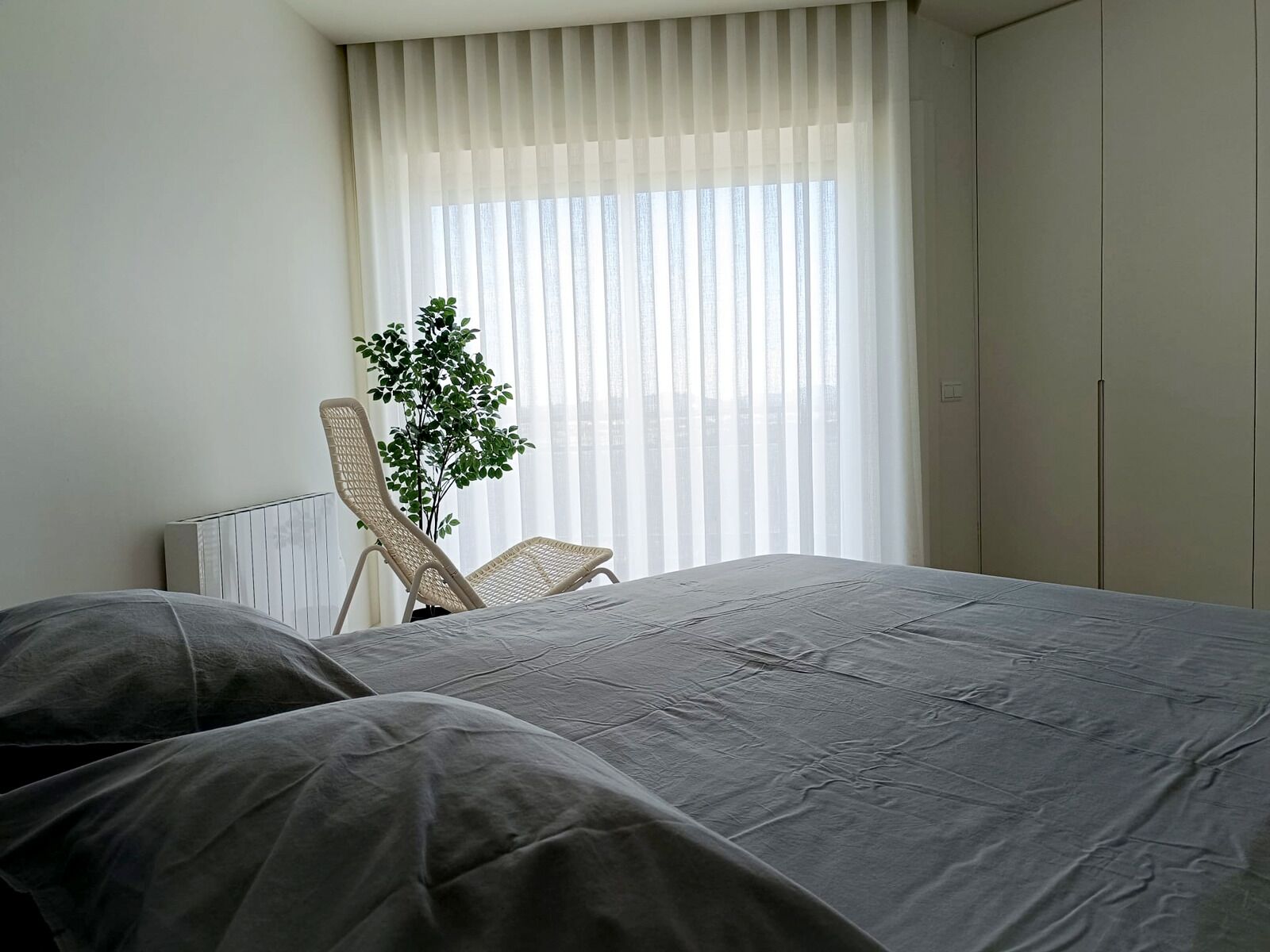A hotel room with a bed, a chair, and a window with blinds.