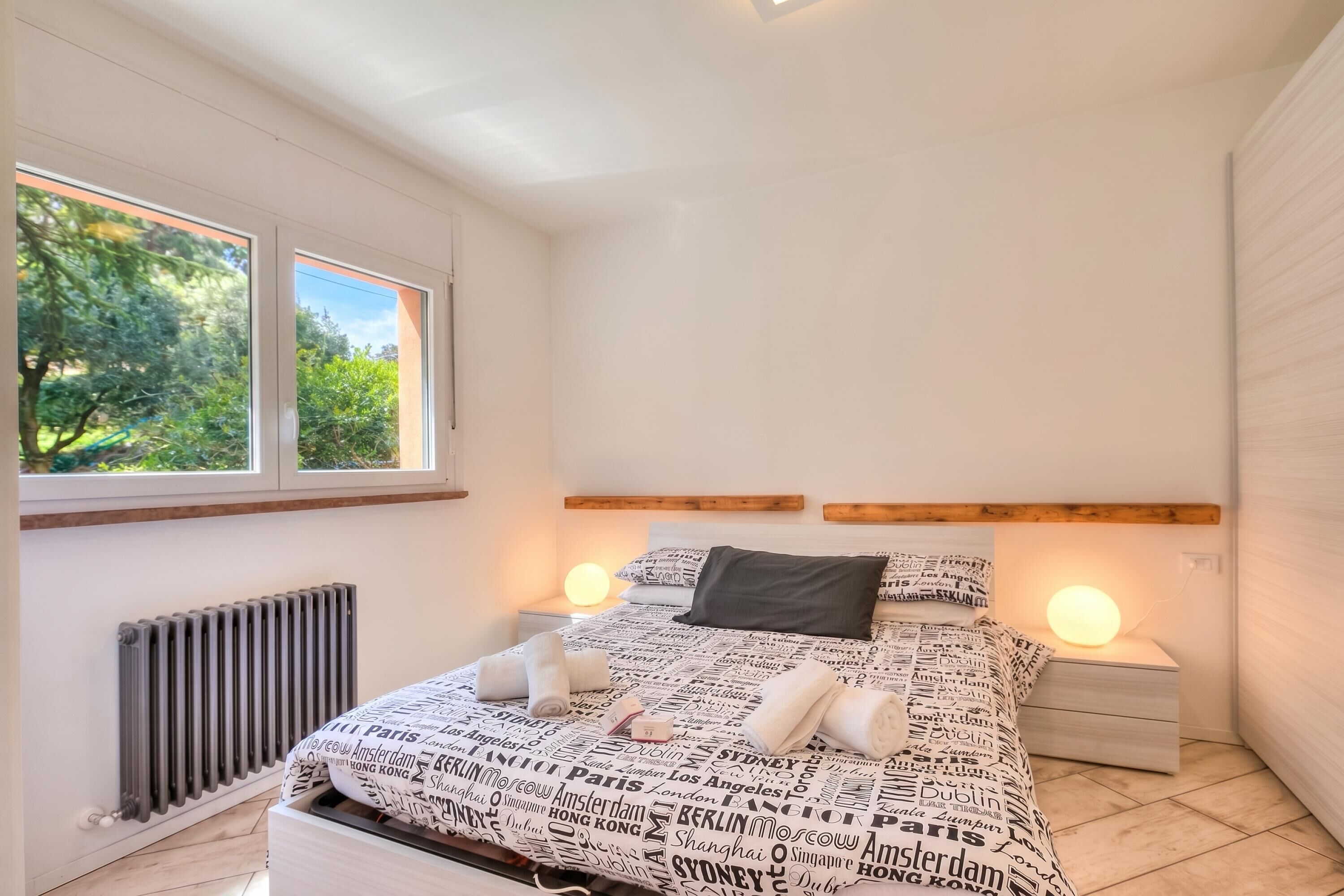 Un dormitorio con cama, dos mesitas de noche, una ventana y un radiador.