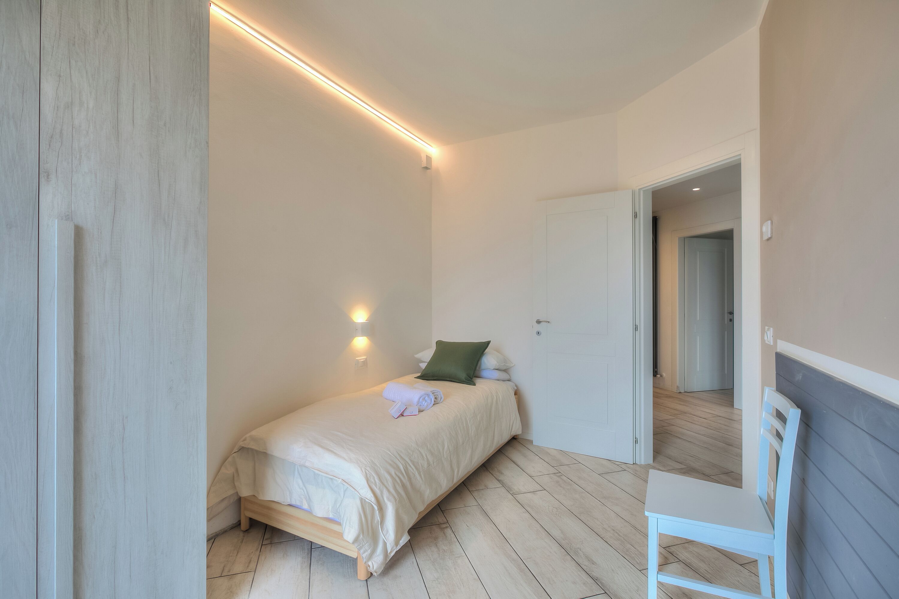 A bedroom with a bed, a chair, and a door leading to another room.