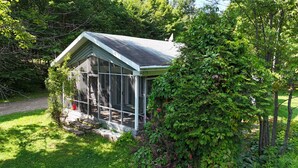 A small glass-enclosed structure with a sloped roof, surrounded by lush greenery and trees. - Ô Petit Chalet | Retraite en nature by Alchalet (Saint-Raymond)