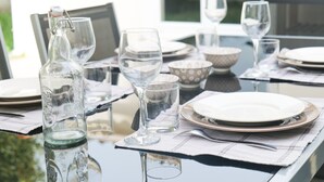A dining table set with plates, glasses, and a bottle, reflecting on the glass surface.
