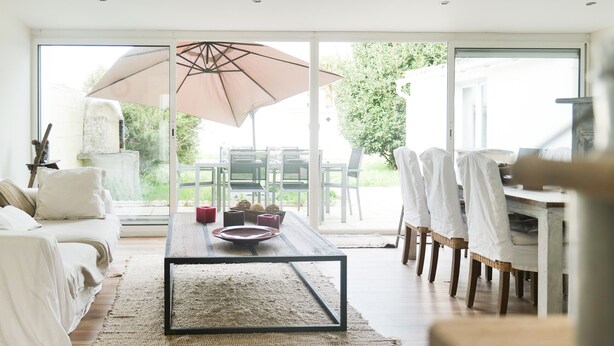 A modern living room with a wooden coffee table, white sofas, and a large sliding glass door leading to an outdoor patio.