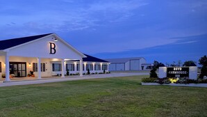 A modern building with a prominent 'B' sign, a covered entrance, and a sign for 'Boyd-Farmhouse-Inn'. - Boyd Farmhouse Inn (DeWitt)