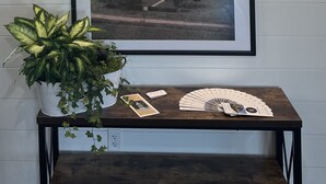 A wall with the text "ALL ROADS LEAD TO THE FARM..." above a framed picture of a farm scene. Below, there's a table with a plant, a framed picture, and some cards. - Boyd Farmhouse Inn (DeWitt)