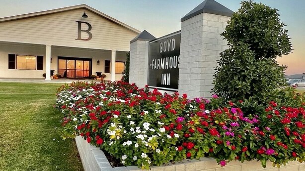 A Boyd Farmhouse Inn with a large 'B' on the building, surrounded by a flower bed with various flowers. - Boyd Farmhouse Inn (DeWitt)