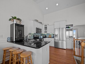 A modern kitchen with white cabinets, stainless steel appliances, a black granite countertop, and wooden bar stools.