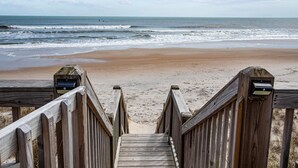 Een houten looppad dat naar een zandstrand leidt, met de oceaan op de achtergrond.