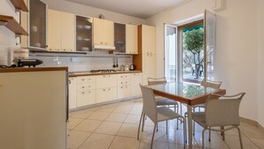 A modern kitchen with white cabinets, a dining table with chairs, and a view through a glass door.