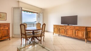 A dining area with a table and chairs, a television on a cabinet, and a view through a door.