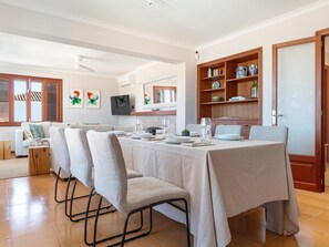 A dining area with a table set for four, chairs, a television, and a bookshelf with decorative items.