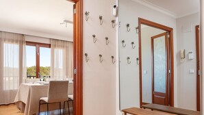 A hotel room with a dining area, a wooden bench, a mirror, and wall-mounted hooks.