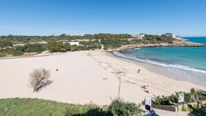 A beach with a clear sky, rocky coastline, and buildings in the background.