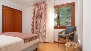 A bedroom with a bed, a chair, a window, a door, and a basket.