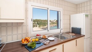 A kitchen with a window view of a beach, a sink, and a refrigerator.