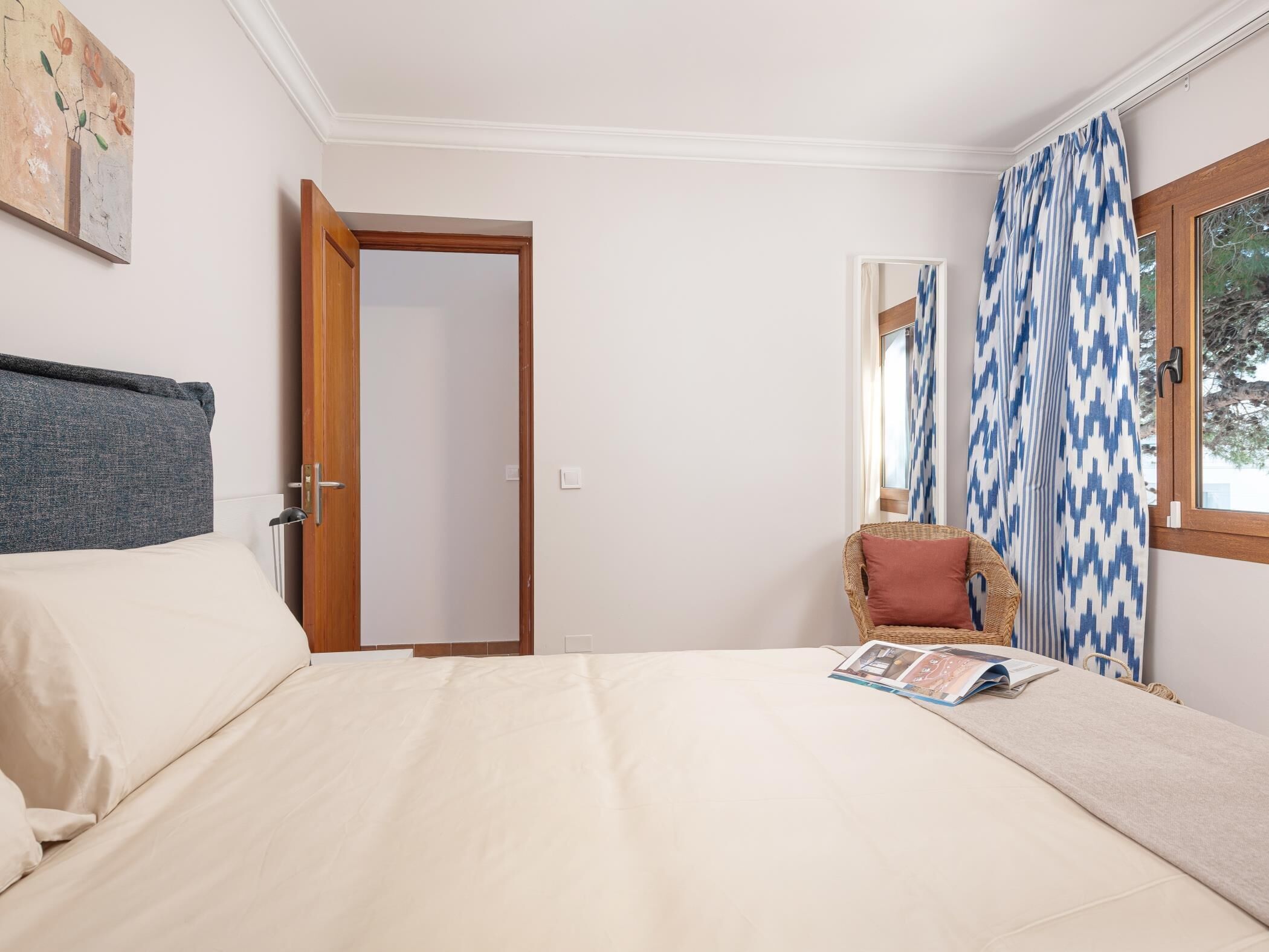 Une chambre à coucher avec un lit, une chaise, une porte, une fenêtre avec des rideaux et un tableau accroché au mur.