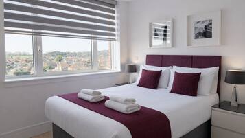 A hotel room with a large bed, two bedside tables, a window with blinds, and a city view.