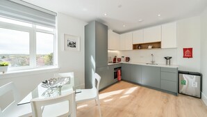Une cuisine moderne avec des meubles blancs, un coin repas doté d’une table en verre et de chaises blanches, et une vue par la fenêtre.