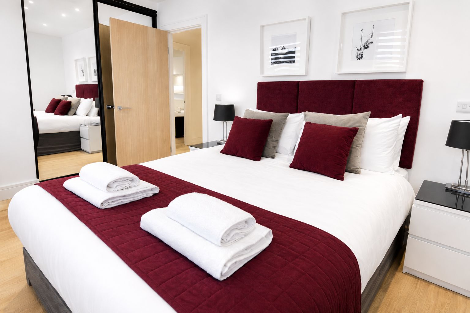 A hotel room with a large bed, a wooden door, a white nightstand, and a mirror.