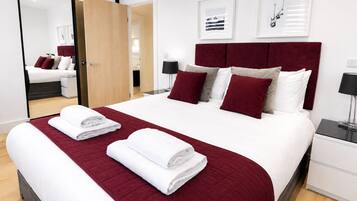 A hotel room with a large bed, a wooden door, a white nightstand, and a mirror.