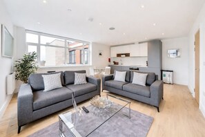 A modern living room with two grey sofas, a glass coffee table, and a large window providing natural light. - Roomspace Apartments - Syward Place (Chertsey)