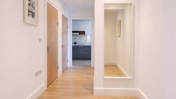 A hallway with wooden flooring leading to a kitchen area with cabinets and a countertop.