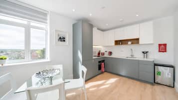 A modern kitchen with white cabinets, a wooden countertop, and a view of the city through a large window.