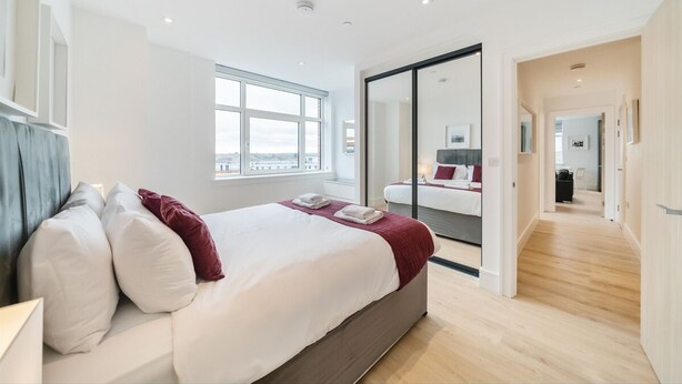 Une chambre d’hôtel moderne avec un grand lit, une vue sur un balcon accessible par une porte coulissante, et un plancher en bois.