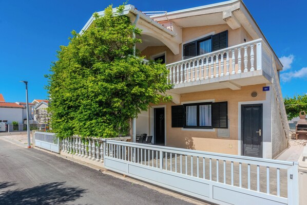 A two-story building with a balcony, a tree in front, and a clear sky. - Apartments Plantosar (Vir)