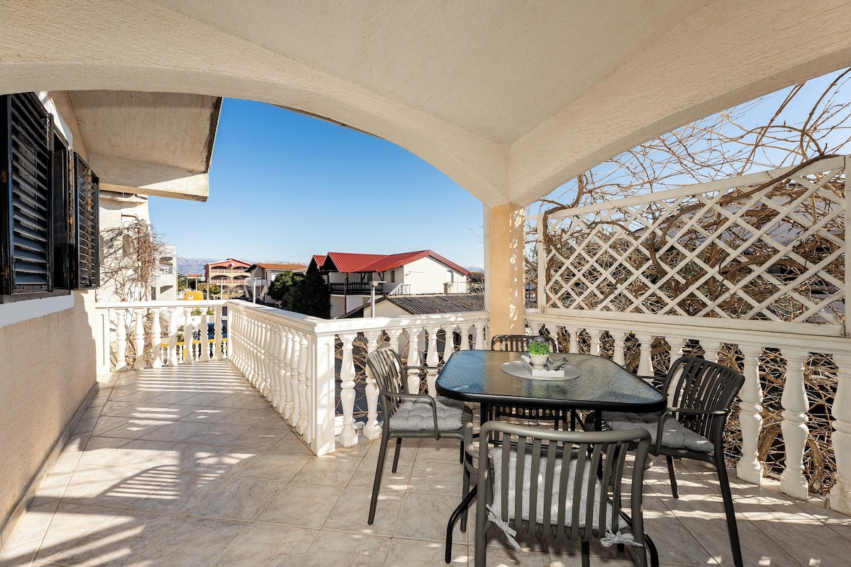 A covered outdoor patio with a table and chairs, a white lattice fence, and a view of houses in the background.