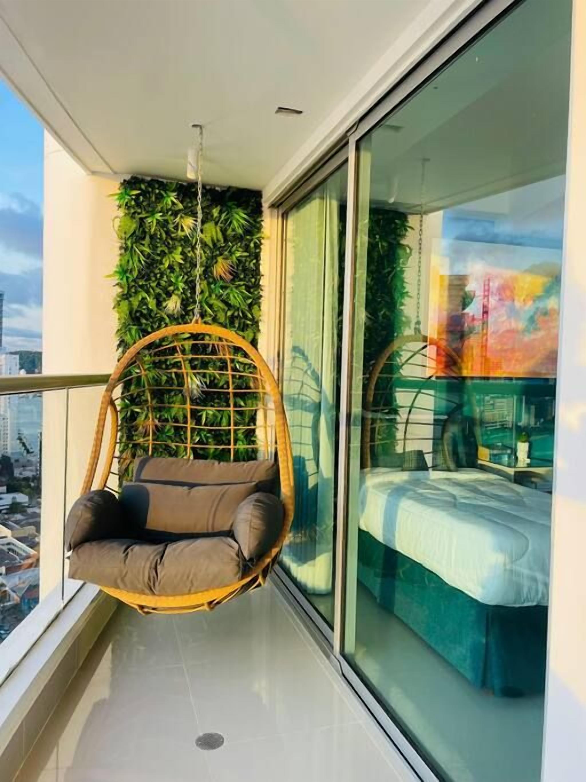 Een balkon met een hangstoel, een bed met een blauwe spreidek en uitzicht op de stad.