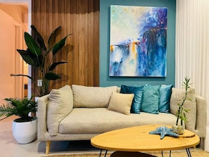 A living room with a beige sofa, a round wooden coffee table, and a large abstract painting on the wall. - SPECTACULAR Jewel @ Palmetto Eliptic Bocagrande 34th Floor (Cartagena de Indias)