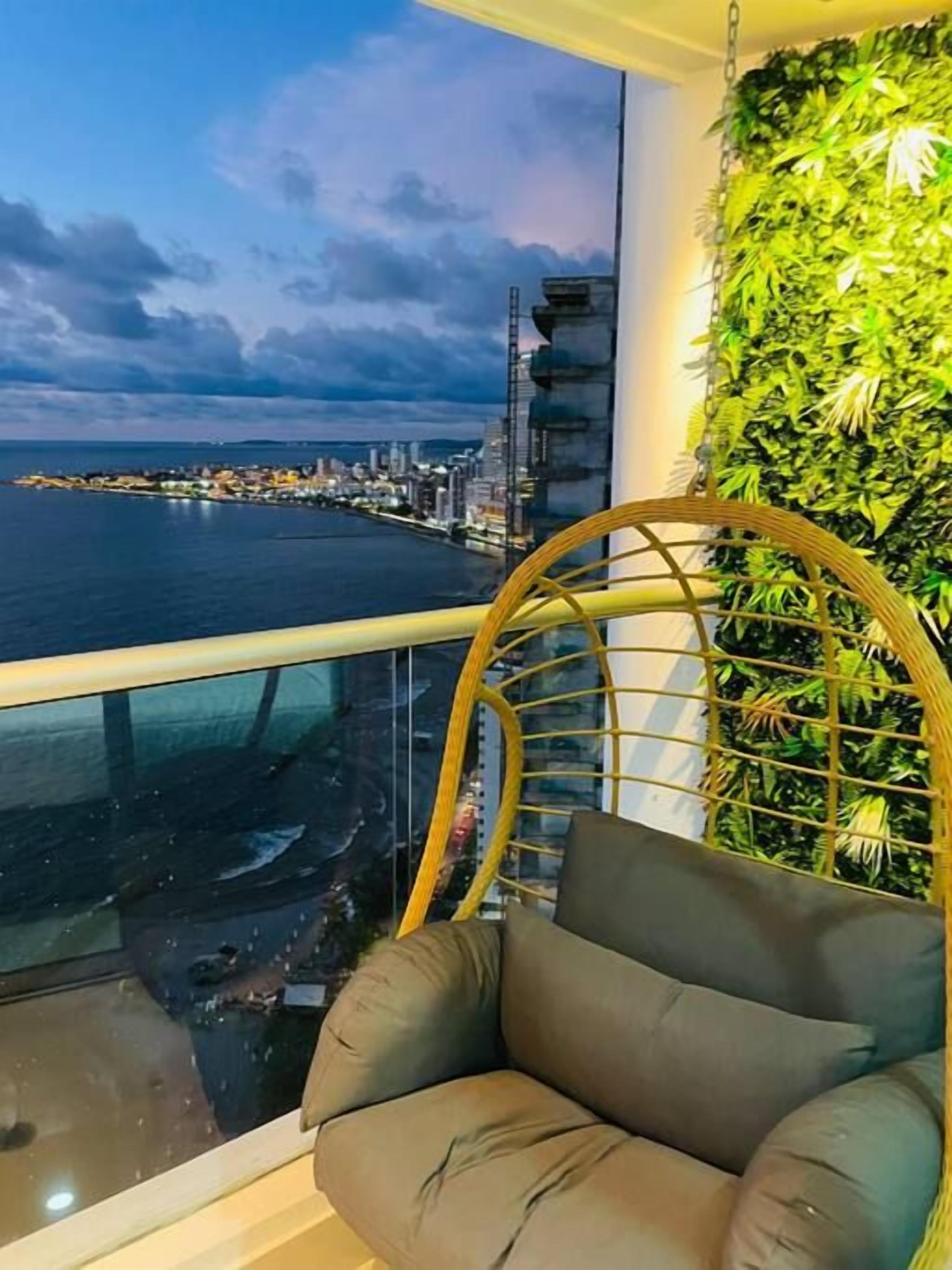 A balcony with a view of a city skyline, a hanging chair, and a green wall.
