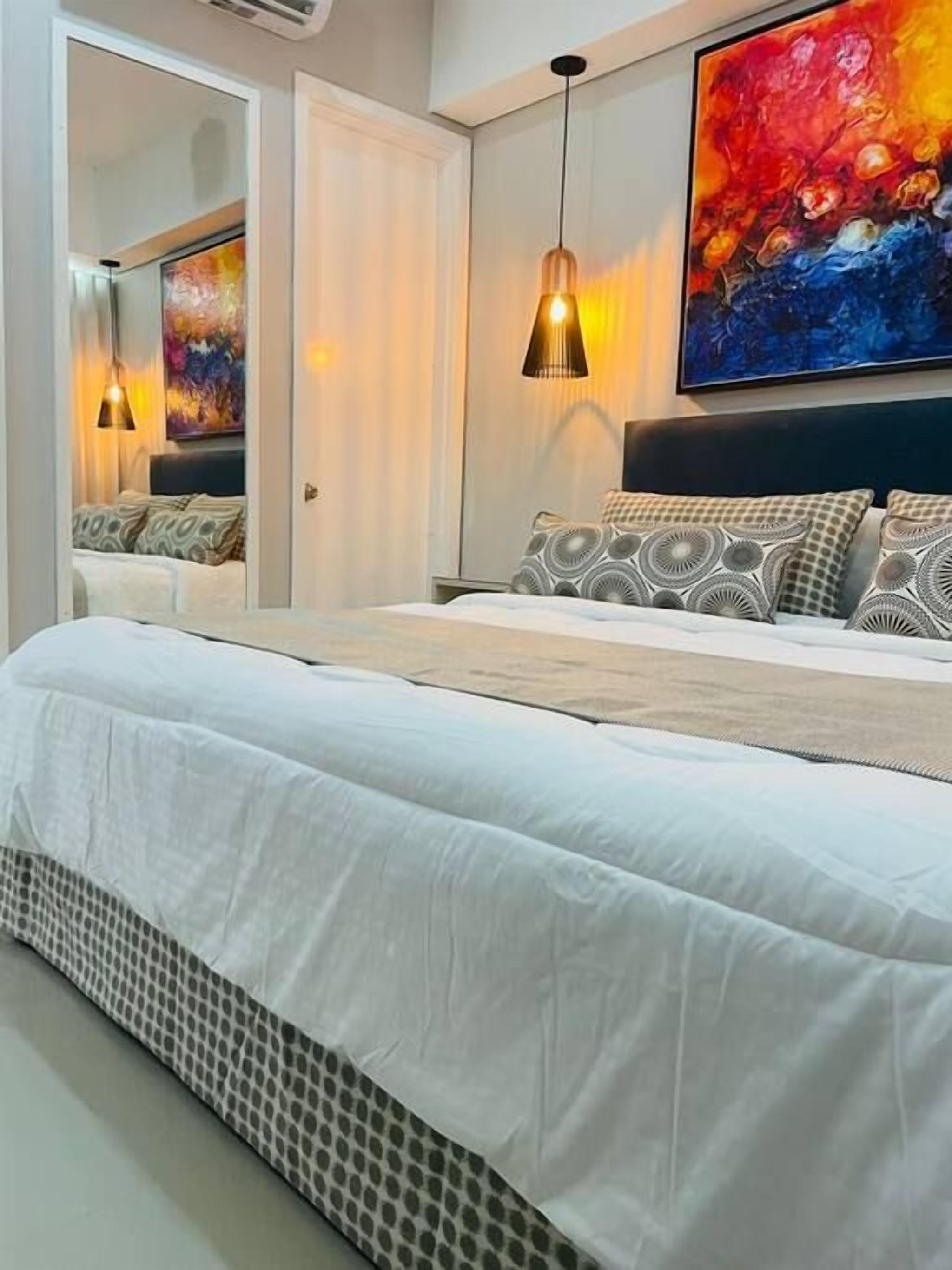 A bedroom with a bed, a large painting, and pendant lighting.