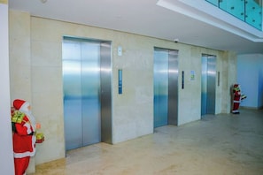 A modern elevator area with four elevators, a marble floor, and a decorative Santa Claus figure.