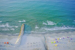 A beach with a long stretch of pebbles leading to the water, a sandy area with umbrellas, and a clear view of the ocean. - SPECTACULAR Jewel @ Palmetto Beach Bocagrande 32th Floor (Cartagena de Indias)