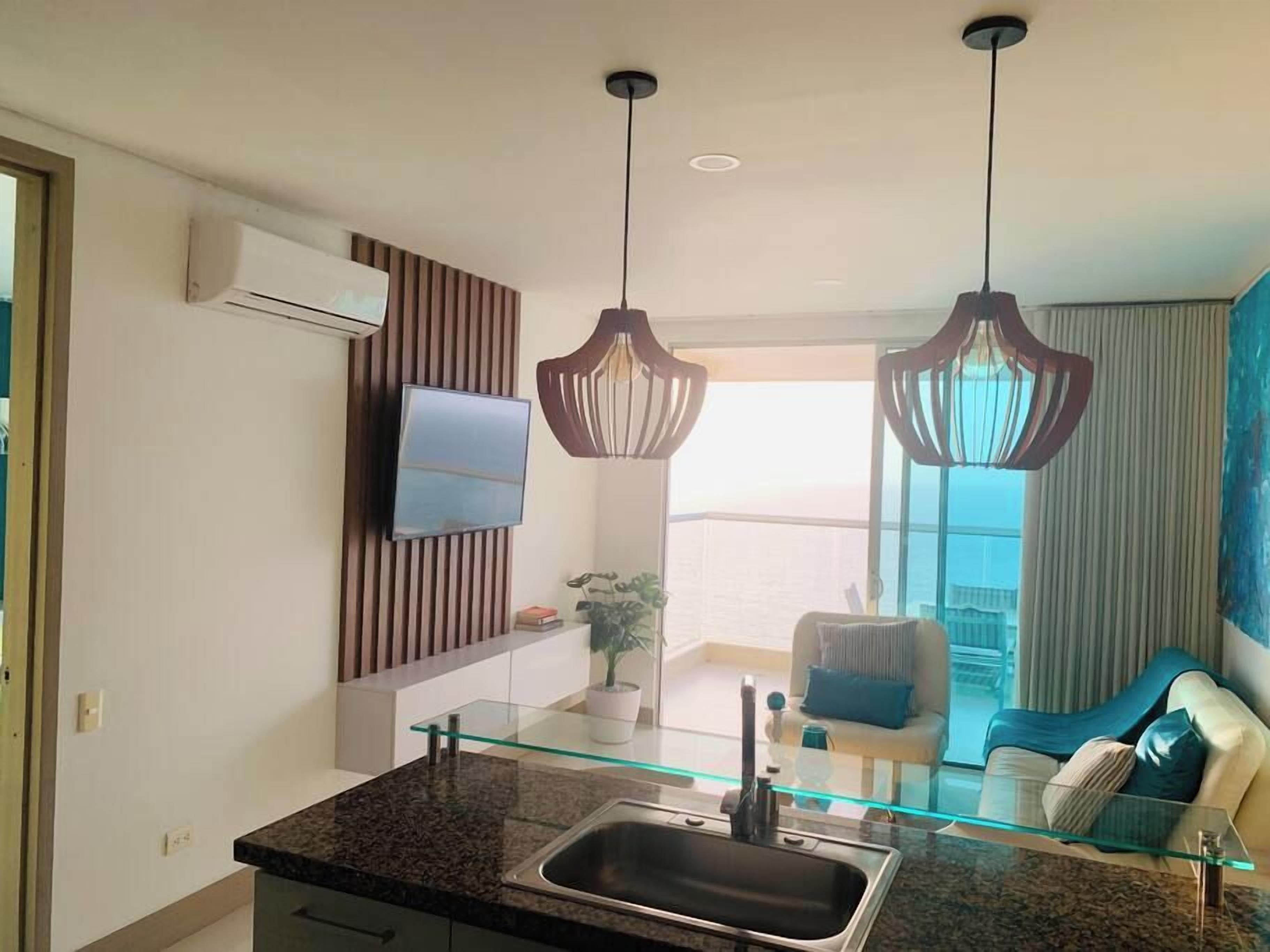 A modern kitchen with a glass countertop, stainless steel sink, and pendant lights.
