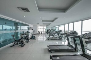 A modern gym with various cardio machines, large windows, and a clean, spacious layout.