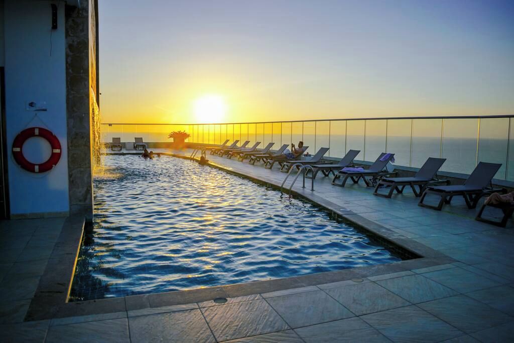 Una piscina iluminada por el sol con sillones de descanso y un flotador.
