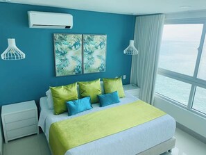 A bedroom with a bed, a nightstand, a wall-mounted air conditioner, a window with a view of the sea, and a painting on the wall. - SPECTACULAR Jewel @ Palmetto Beach Bocagrande 32th Floor (Cartagena de Indias)