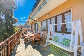 A balcony with a wooden table and chairs, a white swing, and a view of the surrounding area.