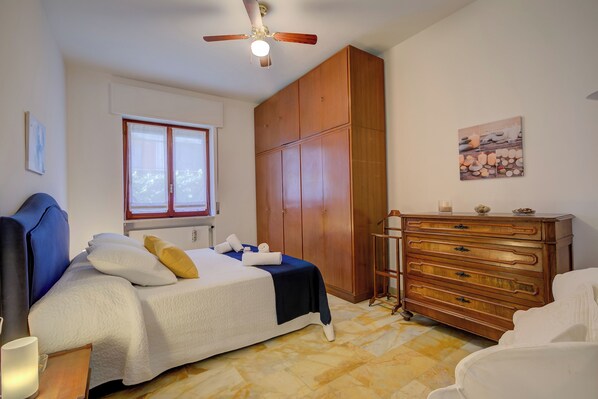 A bedroom with a bed, a wardrobe, a dresser, a ceiling fan, and a window.