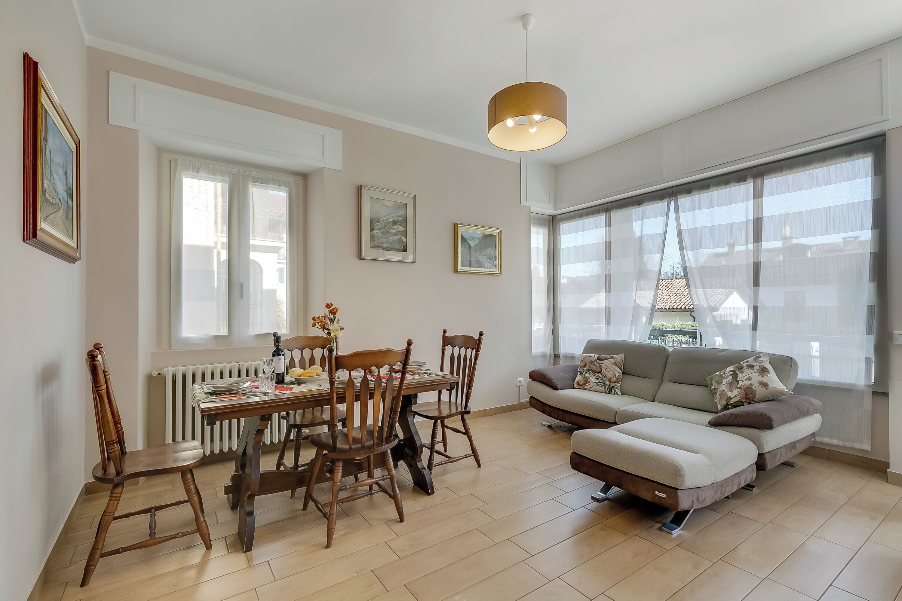 Una sala de estar moderna con comedor, ventanas amplias y una lámpara colgante.