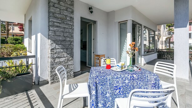 A balcony with a table set for two, a stone wall, and a view of the neighboring buildings. - Il Giardino Di Dante Stresa Center: 2BR Terrace Apartment (Stresa)