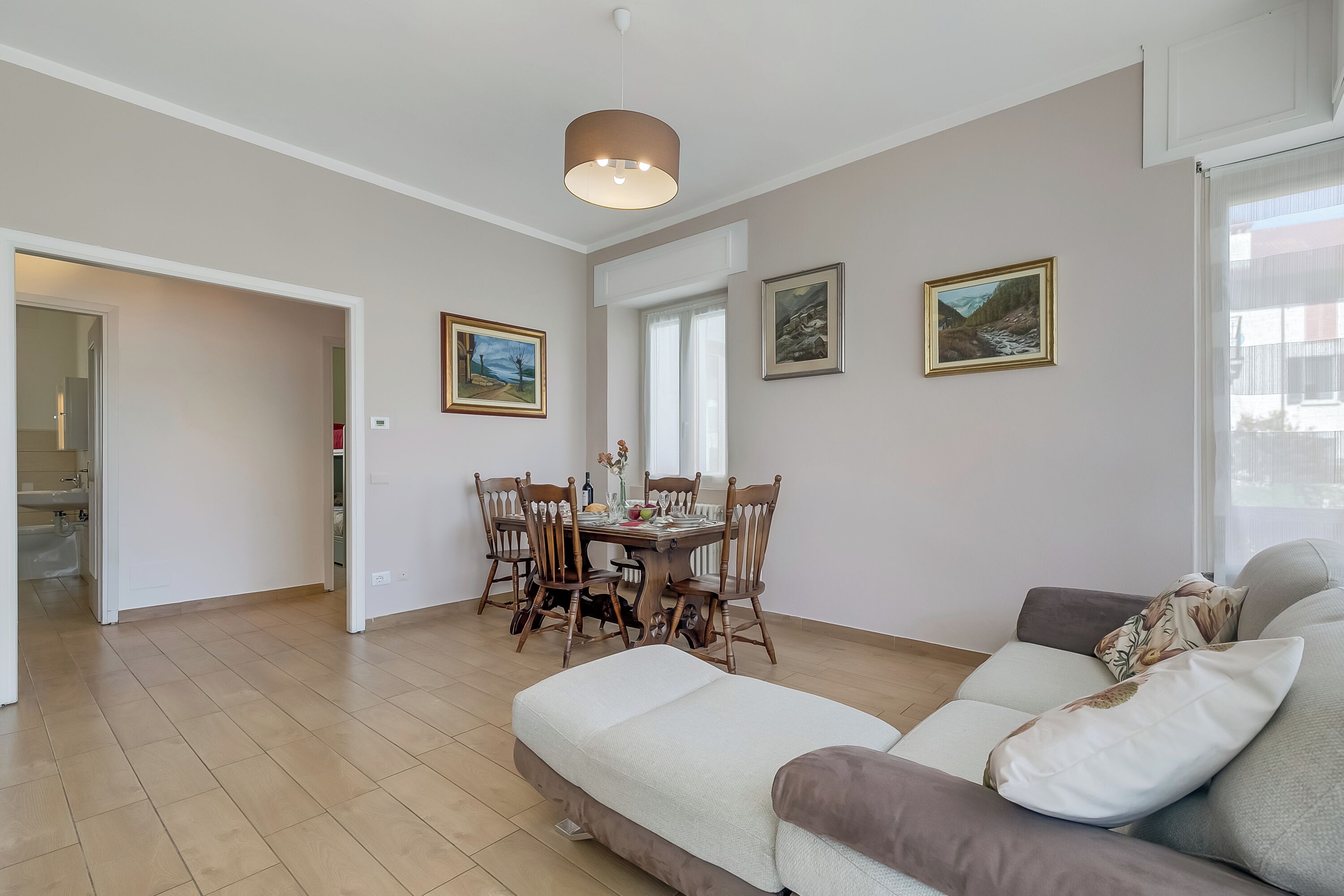 A spacious living area with a dining table, chairs, a sofa, and a ceiling light.