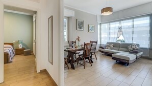 A modern living room with a dining area, a sofa, and a large window providing natural light. - Il Giardino Di Dante Stresa Center: 2BR Terrace Apartment (Stresa)